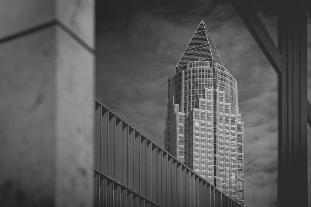 Kristall über der Stadt Der Messeturm – oft fotografiert, selten so gesehen. Eingefasst von moderner Architektur und geometrischen Linien wird er hier zur Bühne einer fast surrealen Ruhe. Die Form erinnert an einen geschliffenen Kristall, der aus dem Stadtgeflecht wächst – ein Symbol für die vertikale Kraft Frankfurts. Dieses Bild verdichtet Perspektive, Rhythmus und Licht zu einer Hommage an die Formensprache der Skyline.