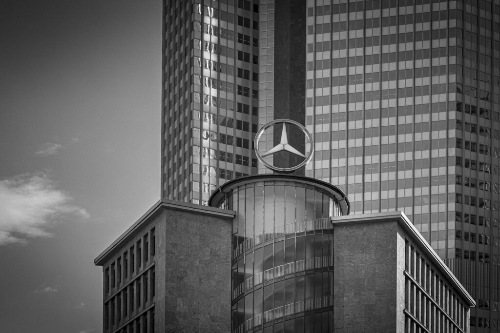 Kreise & Linien Ein architektonisches Stillleben aus Geometrie und Symbolik. Der schwebende Kreis – Sinnbild von Ordnung und Wiederholung – trifft auf die strengen, vertikalen Linien der Fassade. Formale Klarheit und industrielle Kühle verschmelzen zu einem Bild zwischen Präzision und Poesie. Ein Moment urbaner Stille im Zeichen des Übergeordneten.