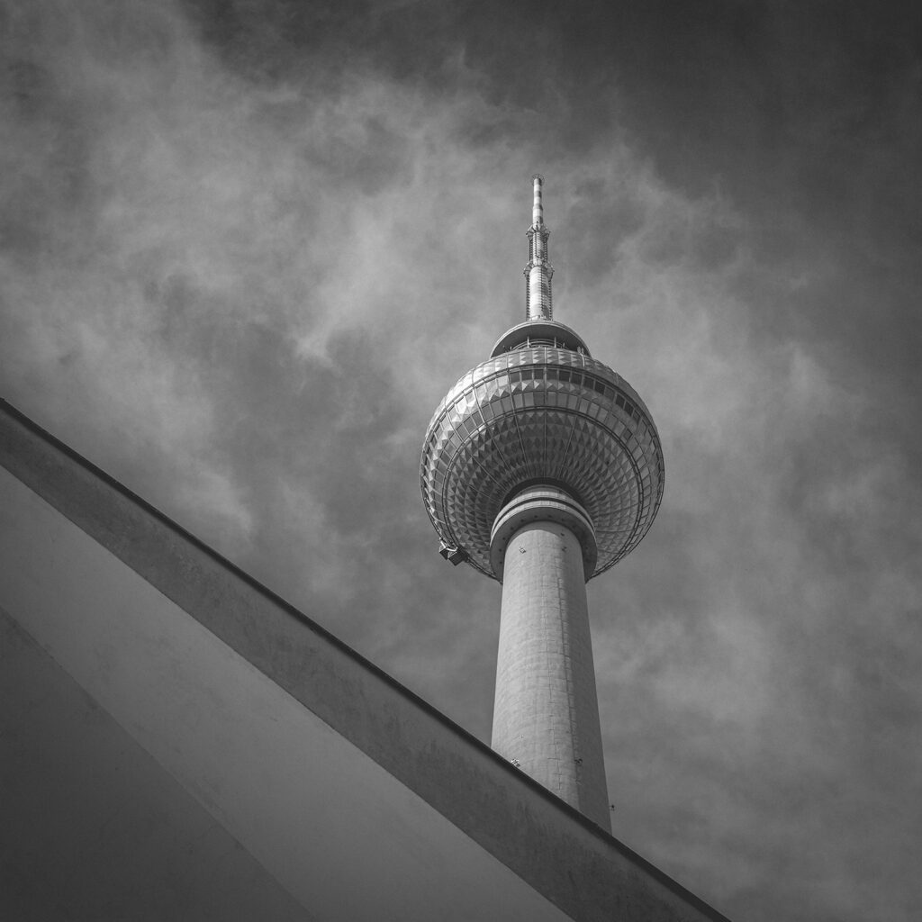 Schwarzweißaufnahme des Berliner Fernsehturms mit grafischer Linienführung und dramatischem Himmel