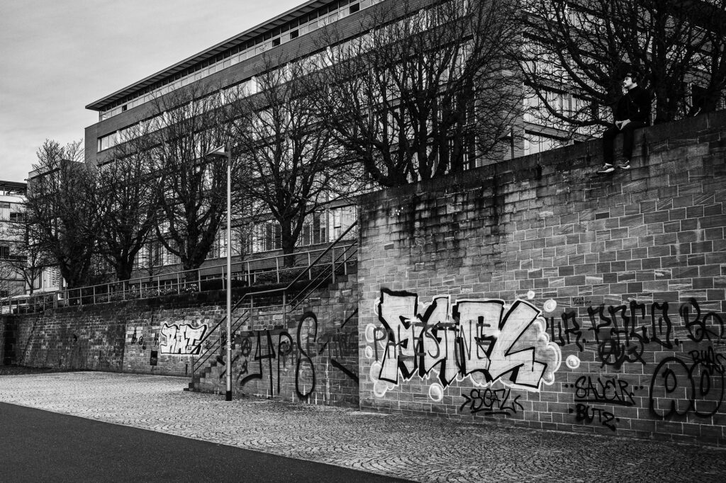 Reflexion: Urbaner Raum In Frankfurts Herzen eingefangen, zeigt dieses Bild die urbane Ruhe. Auf der Mauer sitzend, umgeben von Graffiti - ein stilles Nachdenken in der Stadt der Bewegung. Ein einfaches, aber starkes Bild, das den Betrachter zum Innehalten und Betrachten einlädt.