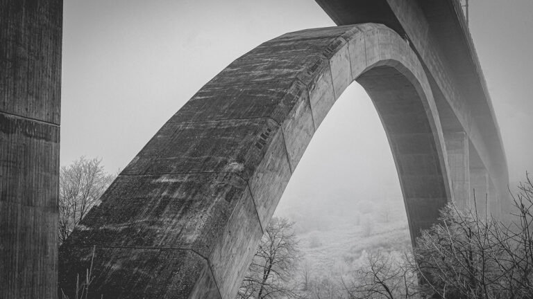 Schwarzweißaufnahme eines massiven Betonbogens der ICE-Brücke bei Limburg im morgendlichen Nebel