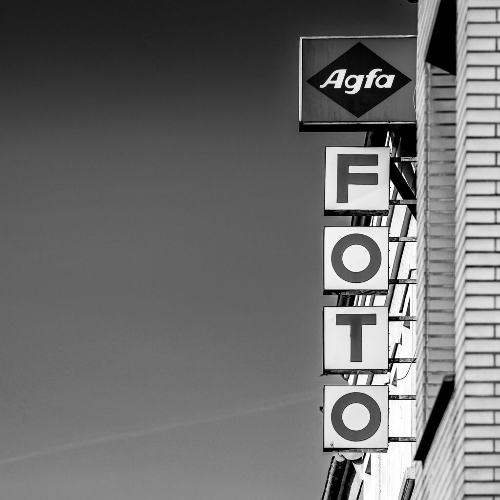 Damals auf Film Schwarzweißfotografie eines alten Agfa-Schildes mit der Aufschrift „FOTO“ an einer Häuserfassade – Erinnerung an die Zeit der analogen Fotografie