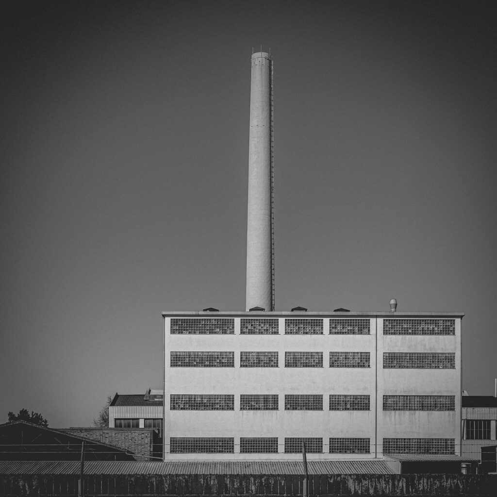 Ordnung und Höhe Schwarzweißfotografie eines Industriebaues mit strengem Raster und hohem Schornstein, der vertikale Klarheit und Ordnung symbolisiert
