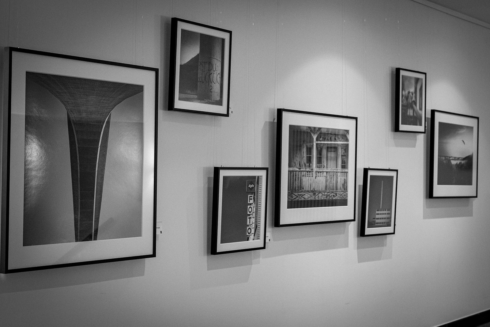Schwarzweiß-Fotografien in schwarzen Rahmen hängen in einer Galerie an einer weißen Wand.