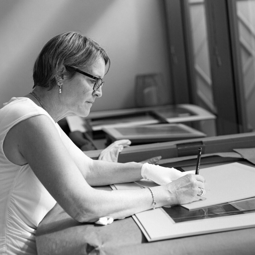 Frau signiert eine gerahmte Fine-Art-Fotografie mit einem Bleistift.