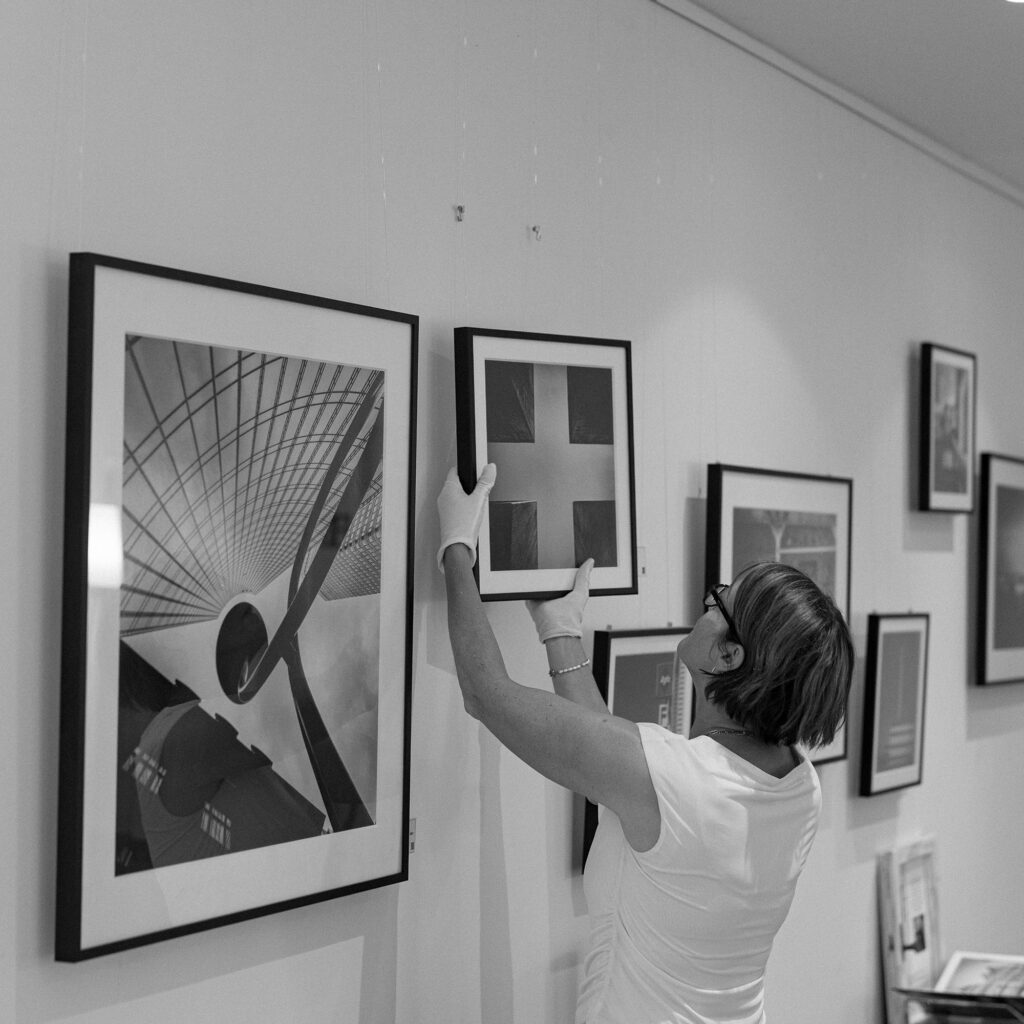 Frau hängt eine gerahmte Schwarz-Weiß-Fotografie an einer Ausstellungswand auf.
