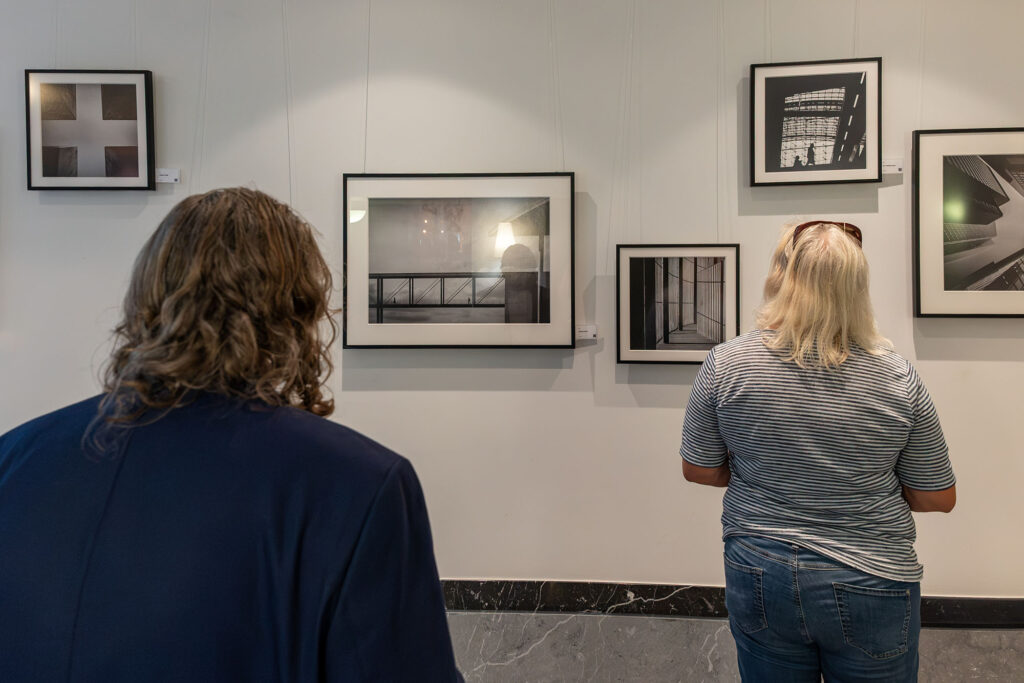 Zwei Besucherinnen betrachten gerahmte Schwarz-Weiß-Fotografien an einer Ausstellungswand.