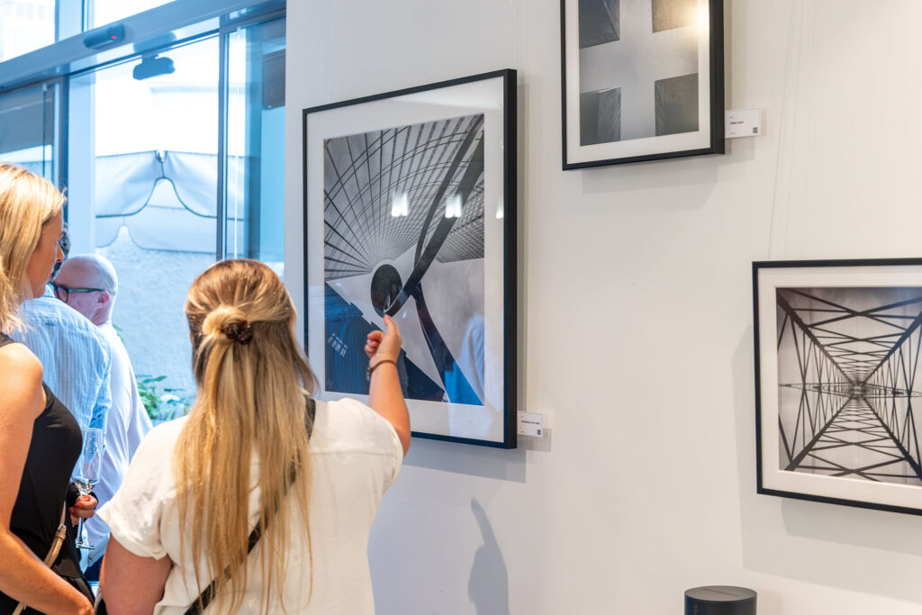 Besucherinnen betrachten gerahmte Schwarz-Weiß-Fotografien an der Ausstellungswand.
