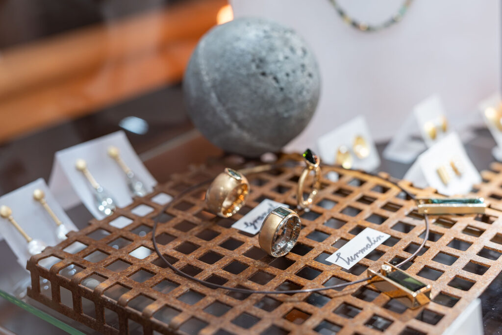 Ringe, Anhänger und weitere Schmuckstücke auf einem Metallgitter in der Ausstellung.