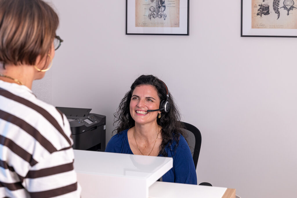 Mitarbeiterin mit Headset im Gespräch mit einer Person am Empfang der Physiotherapiepraxis