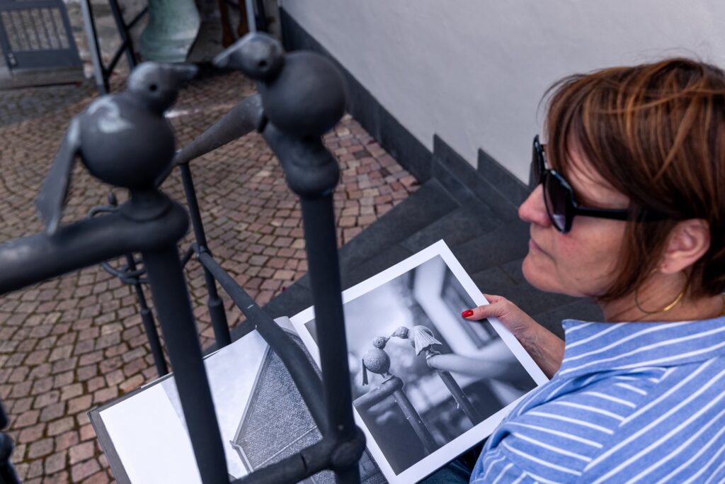 Alexandra Wagner betrachtet im Bildband das Foto der Metallvögel, im Vordergrund die echten Vögel am Geländer