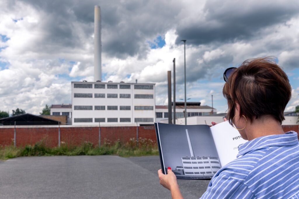 Blick über die Schulter auf den Bildband mit Schornsteinfoto vor dem echten Industriegebäude in Limburg