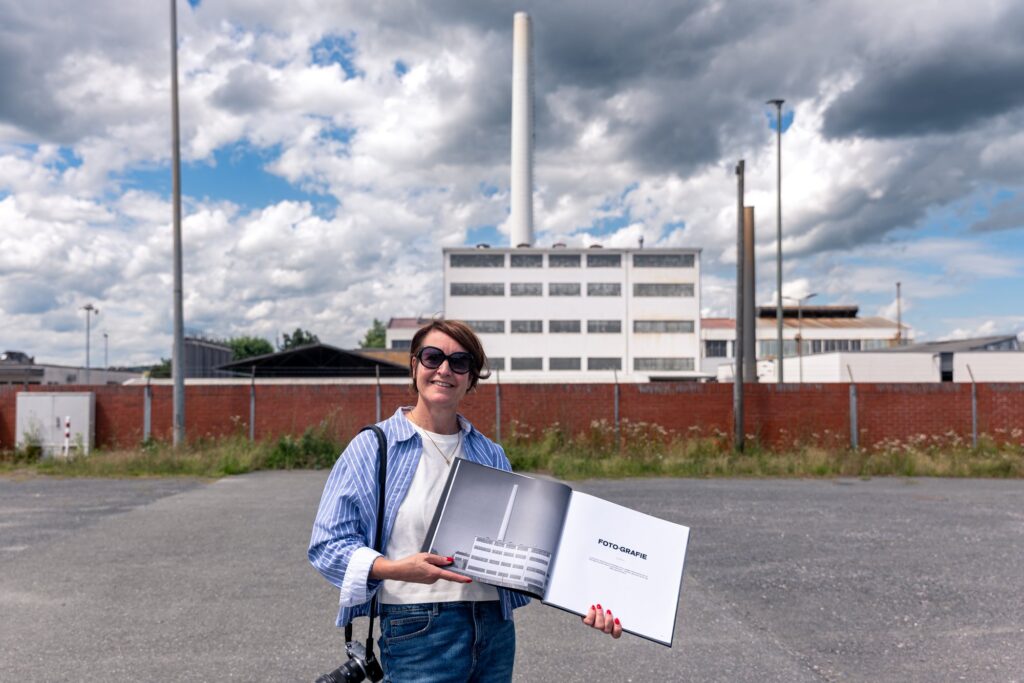 Alexandra Wagner mit Kamera und Bildband vor Fabrikfassade und Schornstein