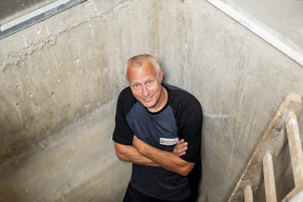 Hausmeister der DAW blickt lächelnd aus dem Pumpenschacht nach oben
