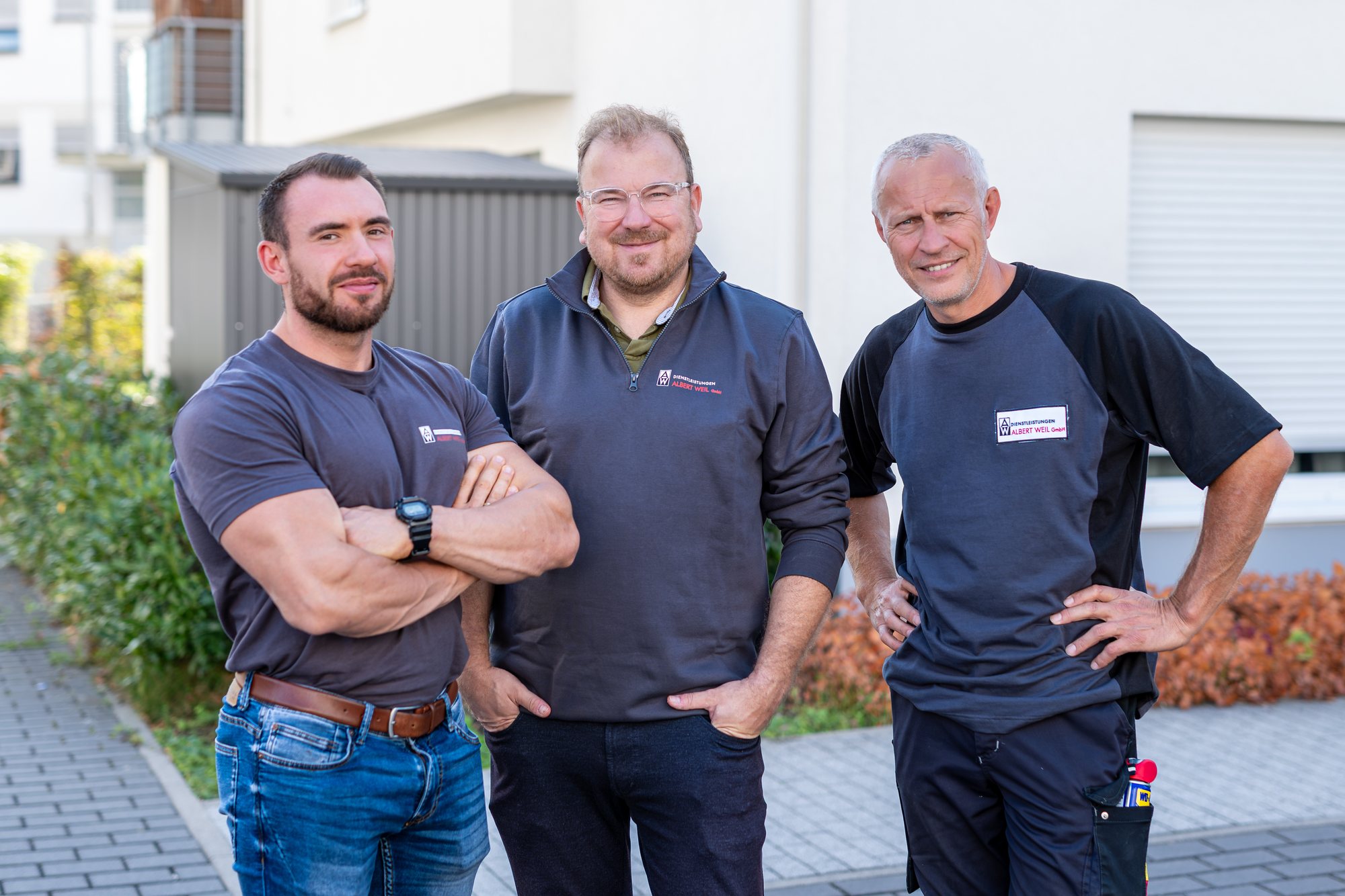 Drei Mitarbeiter des Facility Managements stehen mit verschränkten Armen vor der Wohnanlage