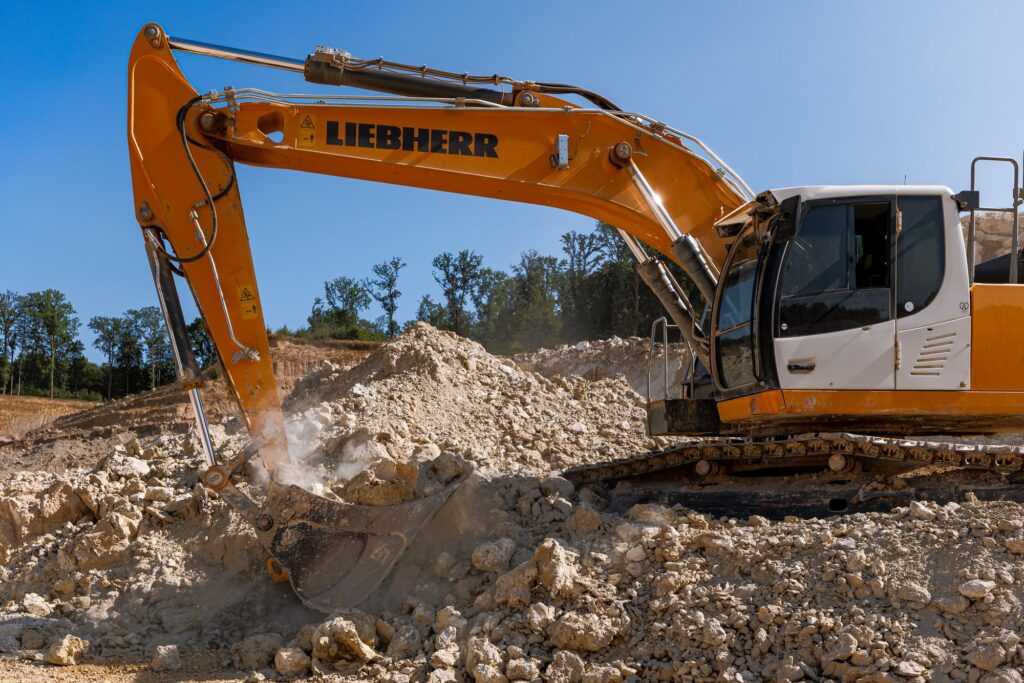Bagger arbeitet im Staub vor einer Tonhalde